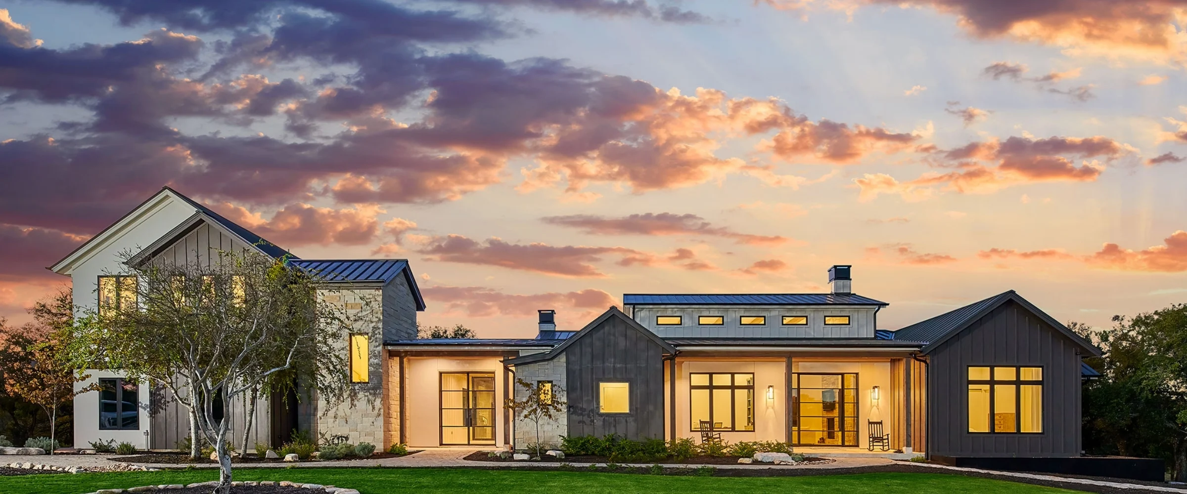 Farmhouse-style home with lit windows under a sunset sky