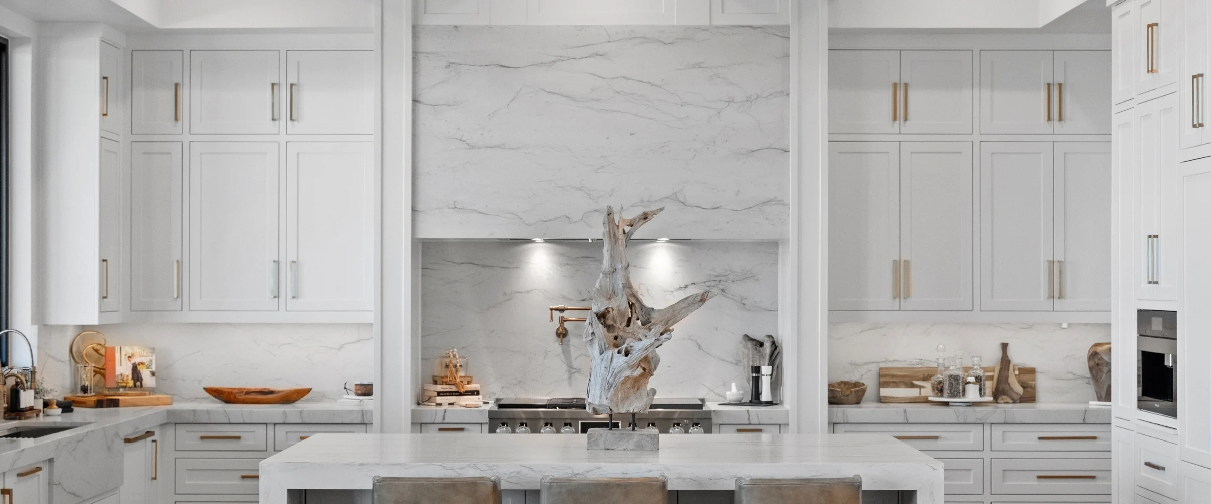 White kitchen with a marble range hood and brass pulls