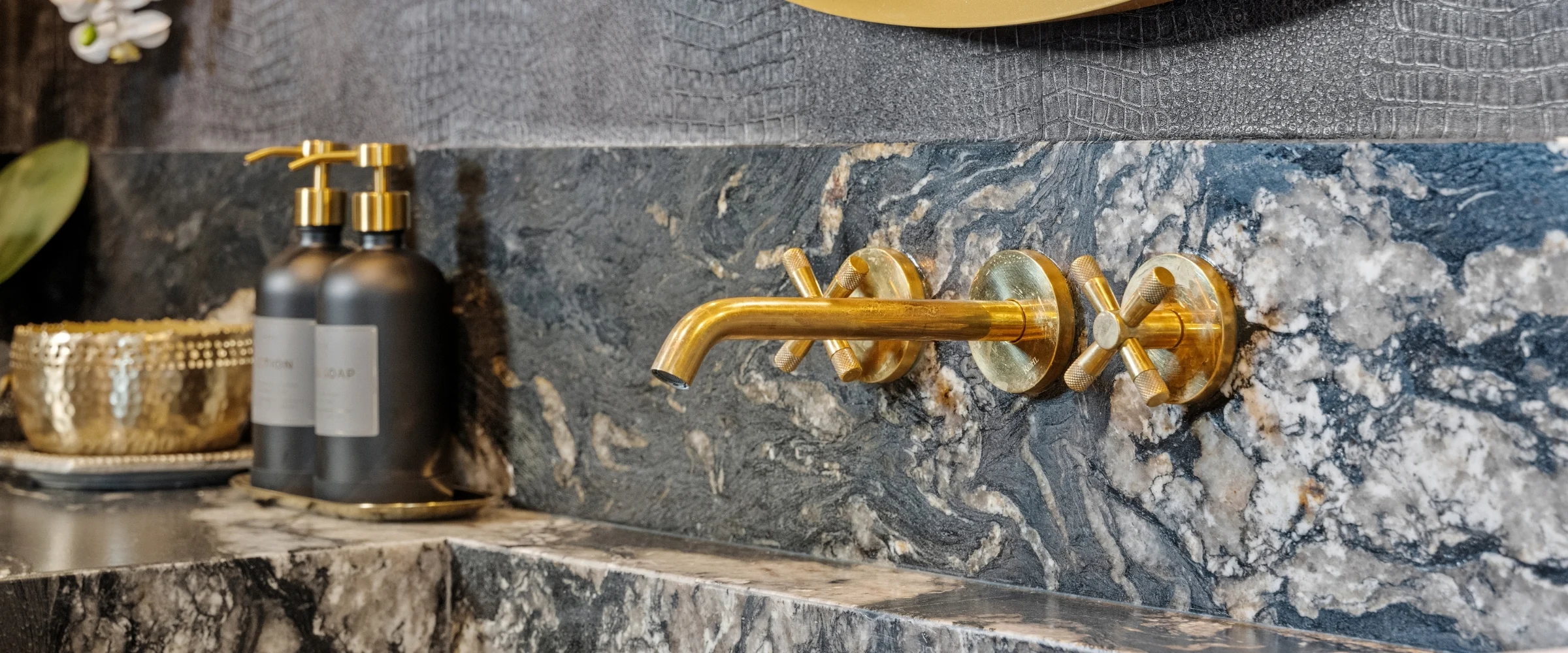 Brass wall-mounted faucet over a dark stone vanity