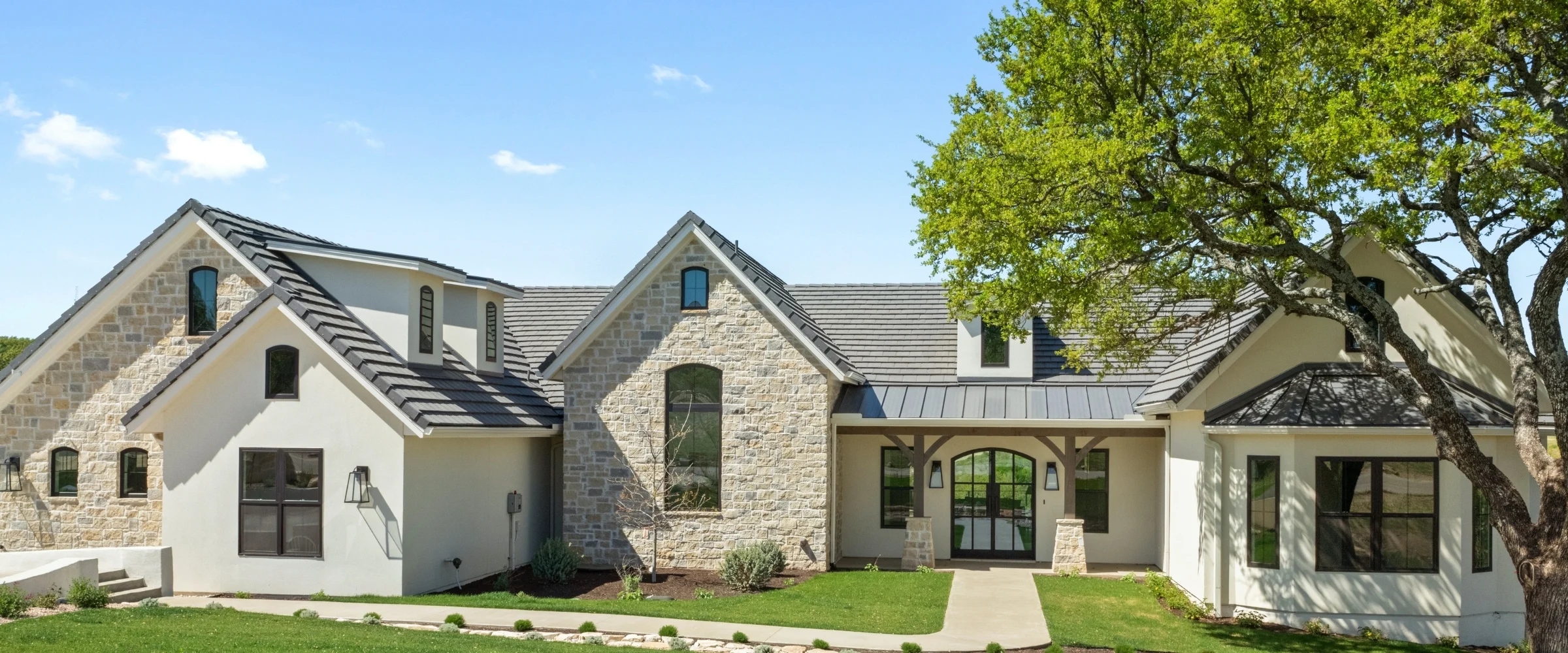 Limestone home with steep gables beneath oak trees