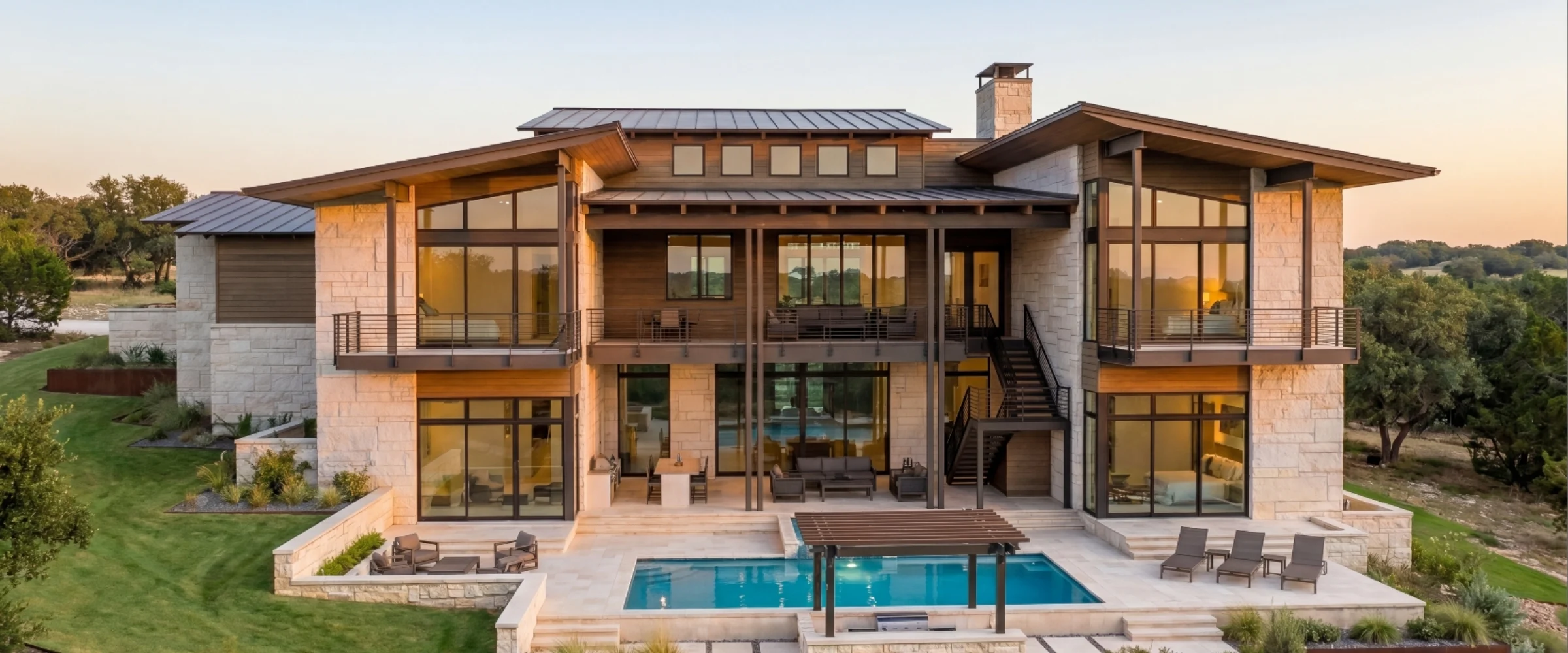 Two-storey stone and timber home with balconies above a pool terrace at dusk